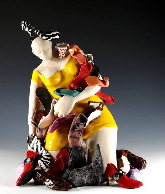 A white figure in a bright yellow dress kneeling in, and clutching, a heap of colorful shoes: red heels, leopard print, zebra stripes, a black boot