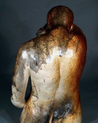 The back of a seated raku figure with head bowed, the pale surface smoked and streaked with rust and black horsehair lines