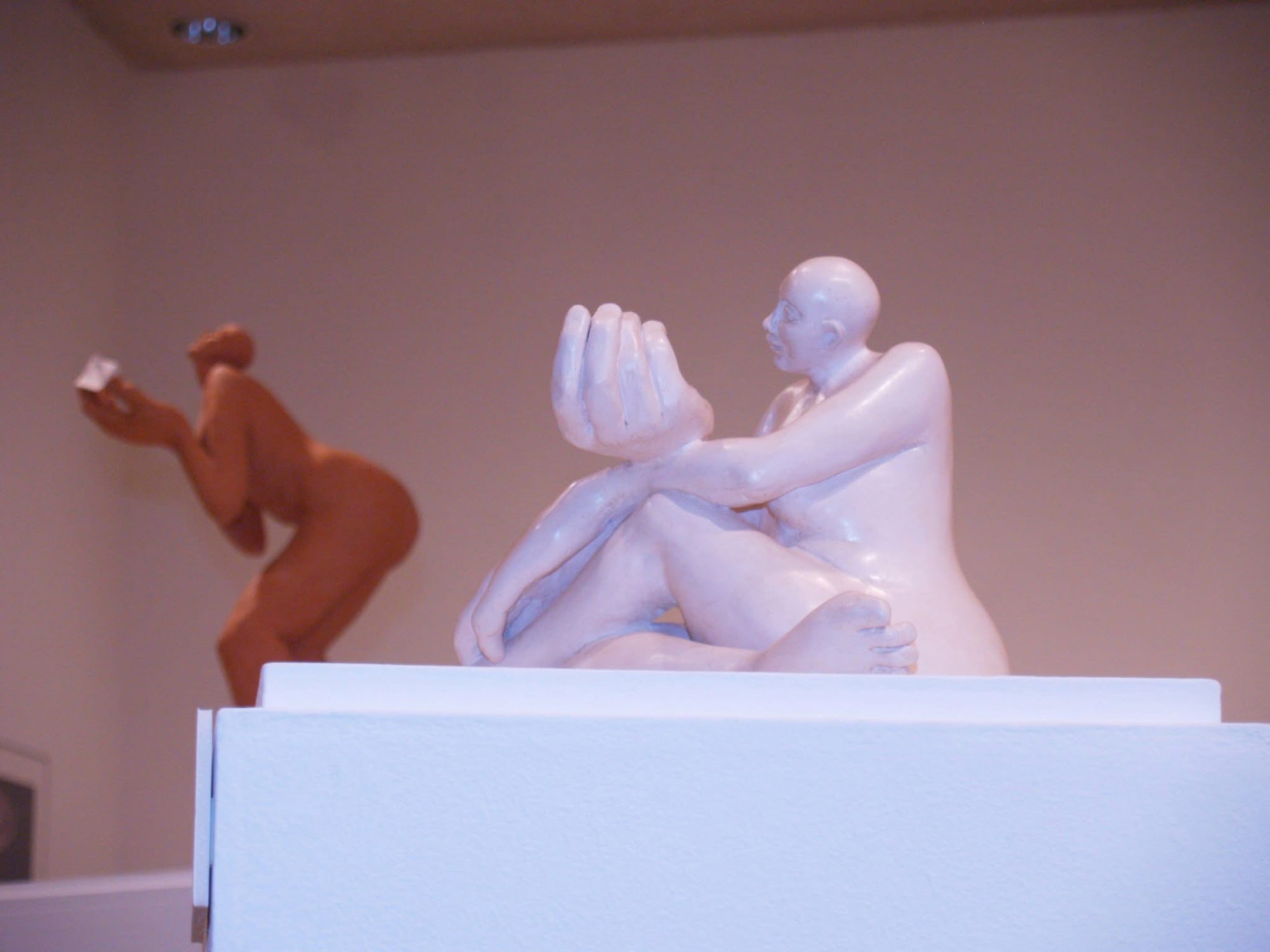 A seated white-glazed figure raising large cupped hands, a bending terracotta figure behind her