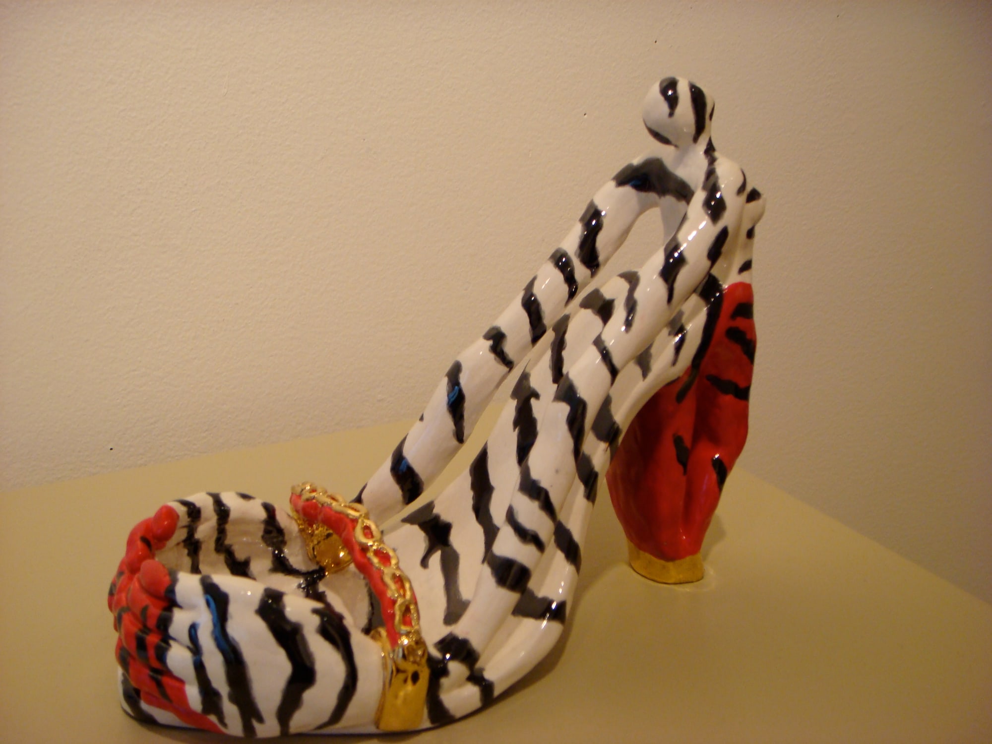 A ceramic stiletto painted in zebra stripes with red toes, a red heel and a gold chain