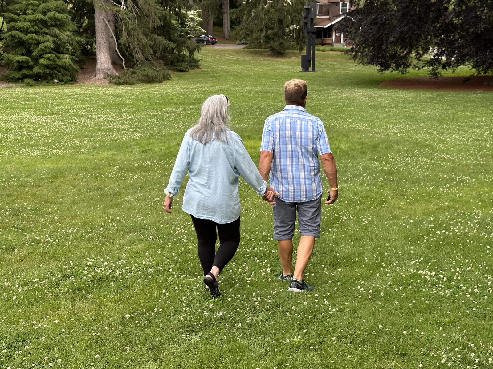 Deborah and her husband walking away hand in hand across a wide green lawn